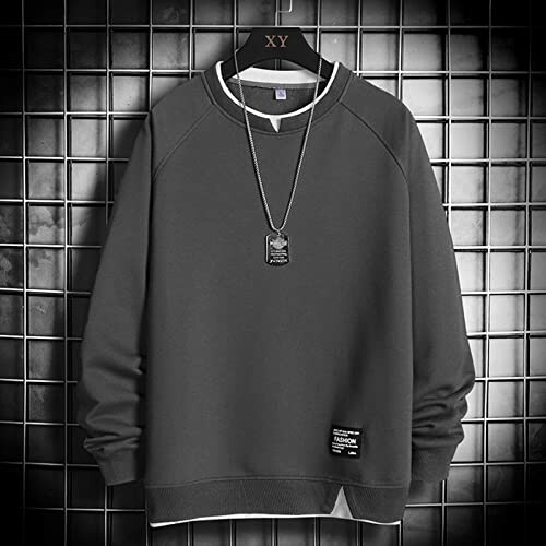 Dark gray sweatshirt with necklace on hanger against a tiled wall.