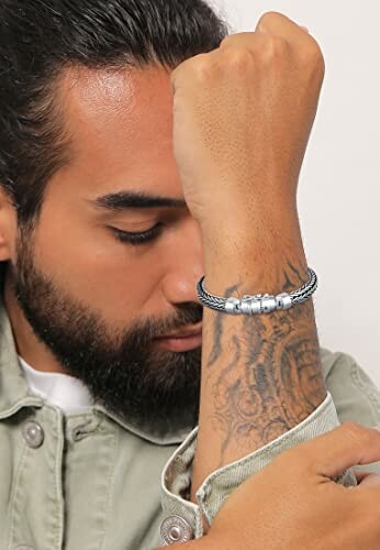 Man wearing silver bracelet with beads and tattooed arm
