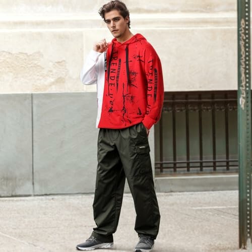 Male model in red hoodie and dark pants standing outdoors
