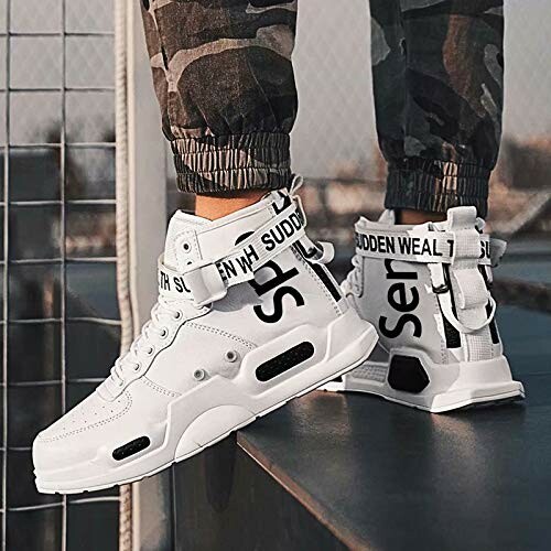 White high-top sneakers with black lettering worn by a person in camo pants.